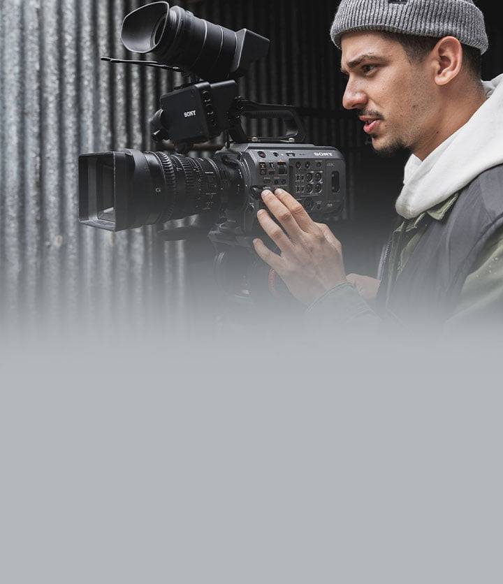 Professional male videographer operating a Sony 4K camera in a studio setting, intensely focused on filming with precise control over the equipment. High-quality video production in action.